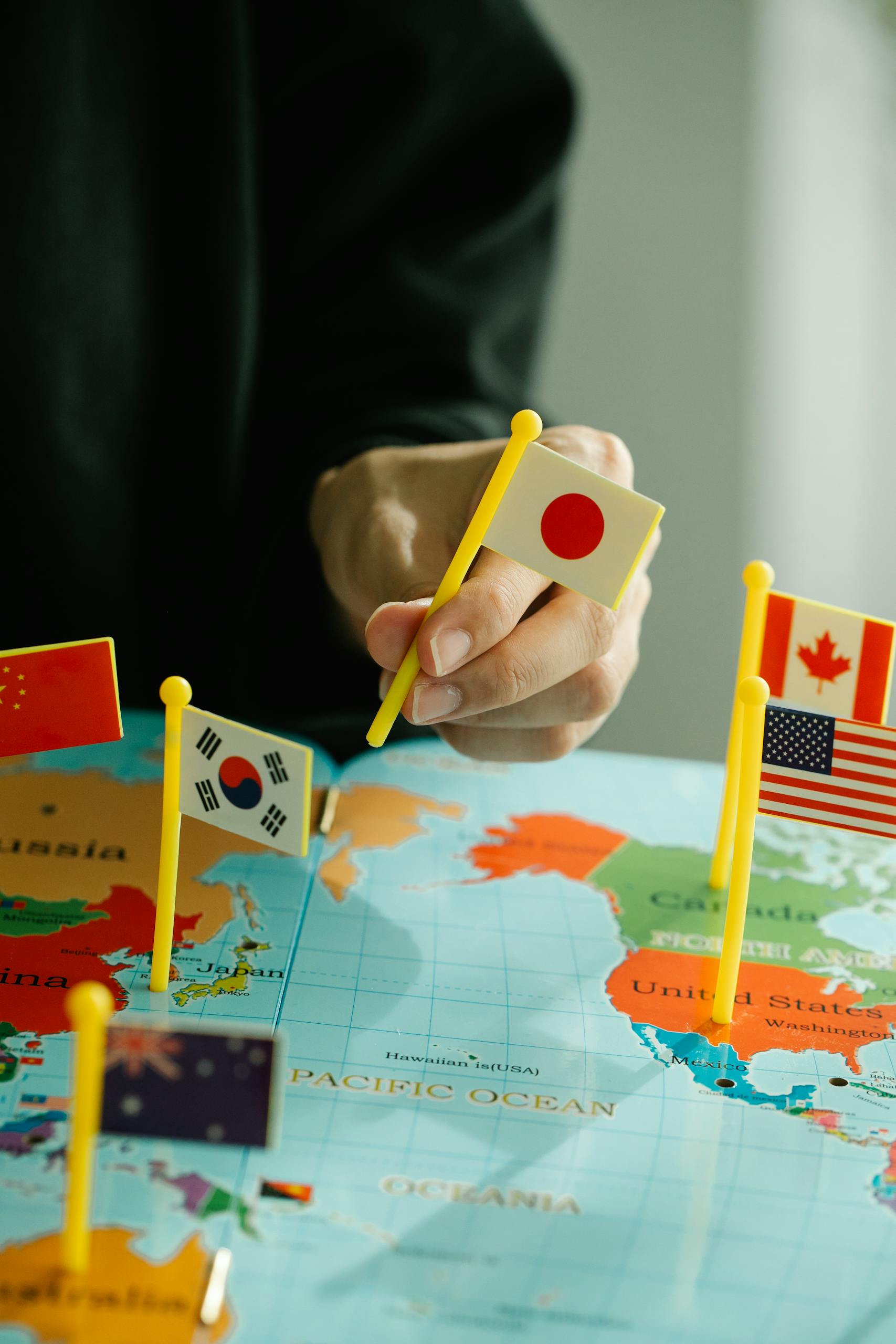Close-up of hand placing Japanese flag on world map surrounded by various country flags.