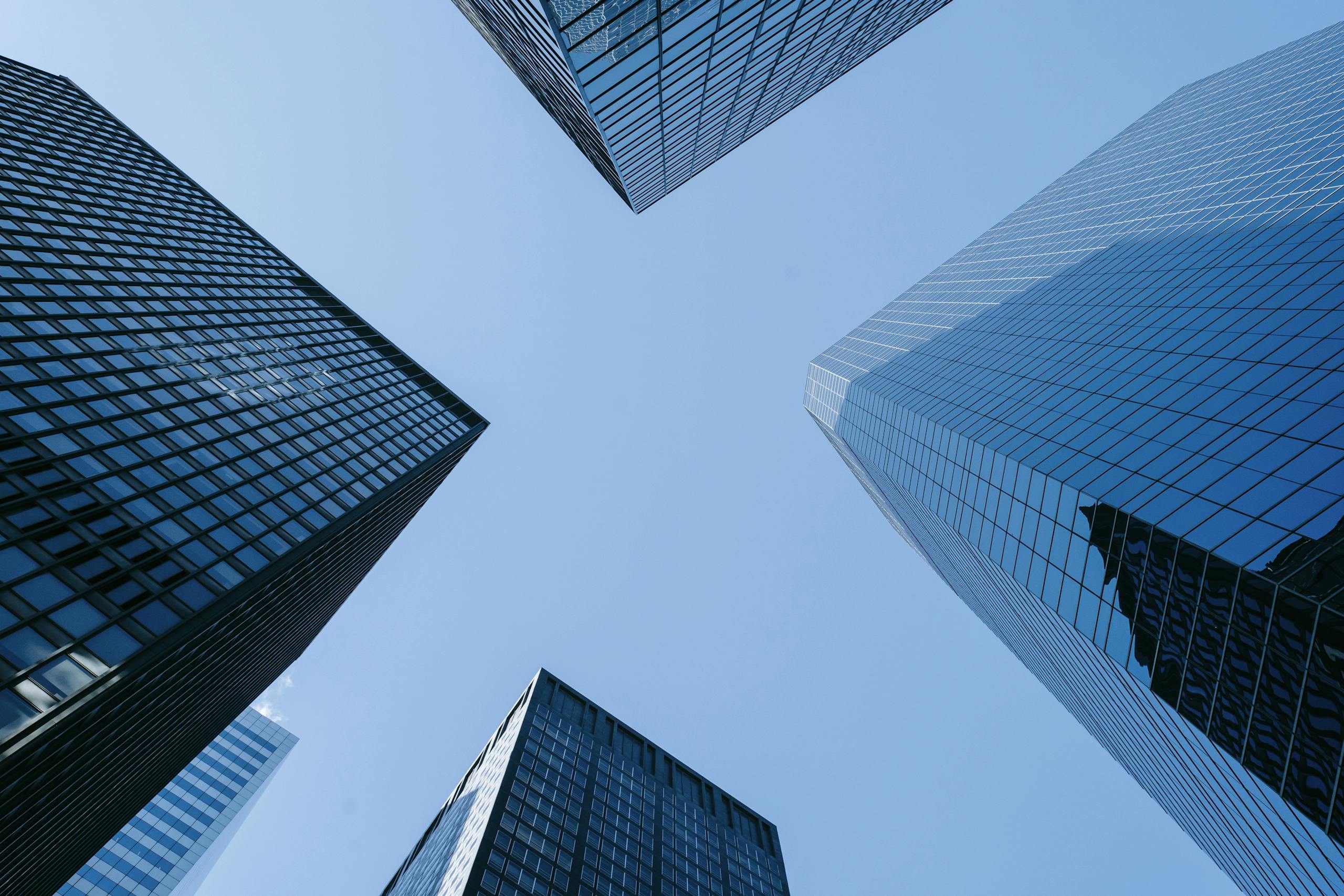 Low angle of high business towers with glass mirrored windows located in megalopolis downtown against blue sky